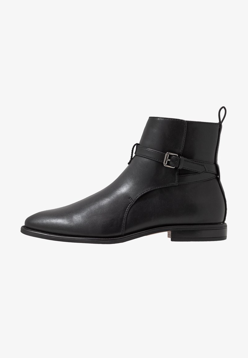 Bottine en cuir noir avec sangle à boucle latérale, talon bas et languette à l'arrière, vue de profil sur fond blanc.