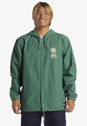 Green hooded jacket made from lightweight material, featuring a palm tree logo and a Quiksilver tag. Elastic cuffs and a button closure.
