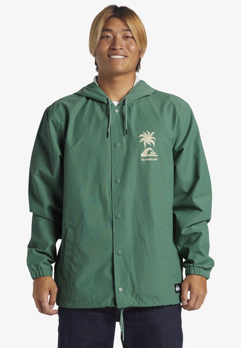 Grøn hættejakke lavet af let materiale, med et palmetræ-logo og et Quiksilver-mærke. Elastiske manchetter og en knaplukning.