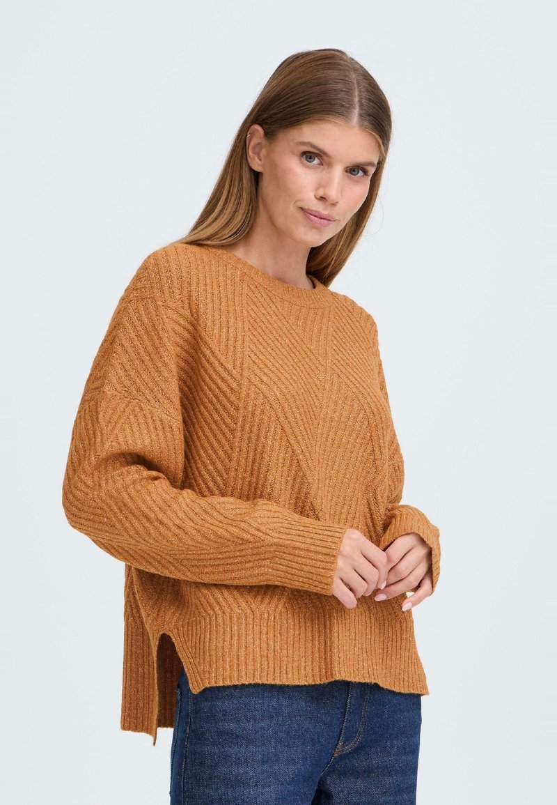 Pull en tricot couleur rouille avec une texture côtelée, présentant un motif diagonal, un col rond et des fentes sur les côtés à l'ourlet.