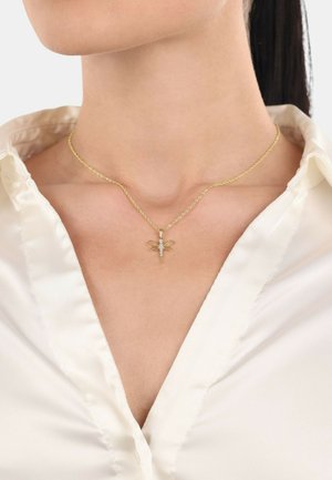 Collana in oro con pendente a forma di libellula, caratterizzata da dettagli intricati e piccole pietre preziose, indossata sopra una blusa di raso bianca.