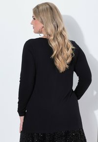 Černý dlouhý rukáv top s měkkou texturou, zakřiveným lemem a uvolněným střihem, v kombinaci s černou sukní posetou flitry. Vlasy stylizované do volných vln.