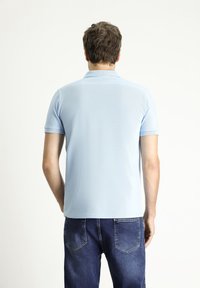 Camisa polo de color azul claro con manga corta y cuello tipo polo, que presenta una textura de tela suave. Combinada con jeans de color azul oscuro.