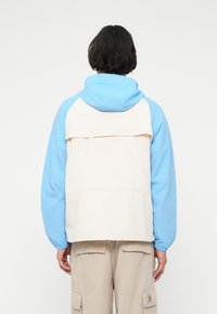 Kapuzenshirt mit blauer und cremfarbener Farbblockierung, aus leichtem Stoff und mit lässiger Passform sowie einer hinteren aufgesetzten Tasche.