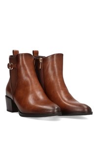 Botas de piel marrón hasta el tobillo con una textura suave, forma afilada y un tacón bajo apilado. Cuenta con una cremallera lateral y acentos decorativos de hardware.
