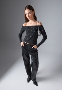 Fekete, vállra húzott pulóver ezüst díszítéssel, fekete bőr nadrággal és hegyes orrú magassarkú cipővel párosítva. Kicsi gyöngyökkel díszített kézitáska.