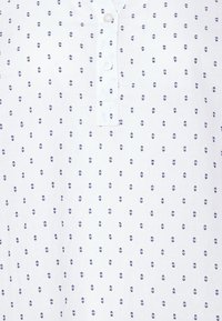 Camicia bianca con una chiusura a bottoni e un piccolo motivo a pois blu navy su tutta la superficie. Il tessuto sembra leggero e ha una consistenza liscia.