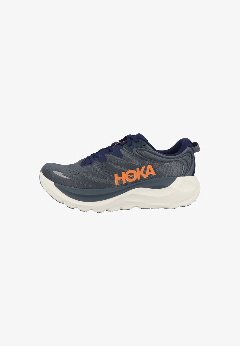 Chaussure de course gris foncé et bleu marine avec une semelle blanche épaisse et un logo "HOKA" orange sur le côté, vue de l'extérieur.