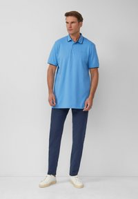Lichtblauwe polo met donkermarine accenten, korte mouwen, een kraag, gecombineerd met donkerblauwe broek en witte sneakers.