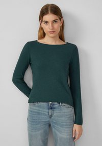 Long-sleeve green top with a wide boat neckline, soft texture, and a relaxed fit. Paired with light blue distressed jeans.