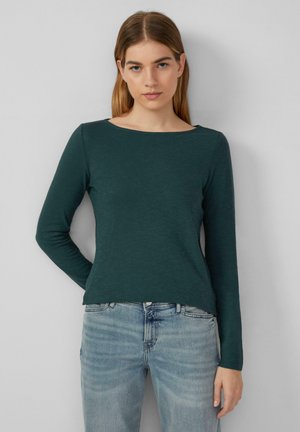 Long-sleeve green top with a wide boat neckline, soft texture, and a relaxed fit. Paired with light blue distressed jeans.