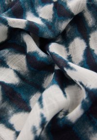 Tkanina w odcieniach niebieskiego i białego z wzorem batiku. Miękka w dotyku i lekka, ułożona w fałdy podkreślające detale materiału.