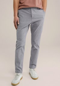 Pelēki, piegriezti bikses, izgatavotas no viegla auduma ar smalku tekstūru; tām ir jostas cilpas un kabatas, apvienotas ar ikdienišķiem baltajiem sporta apaviem.