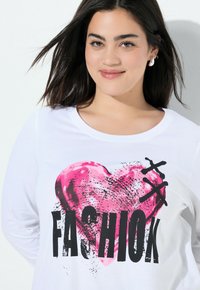 Witte lange mouwen T-shirt met een grote roze hartafbeelding en vetgedrukt zwart tekst die "FASHIOK" zegt. Soepel katoen materiaal en ronde halslijn.