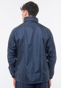 Giacca in nylon leggera di colore blu navy, con maniche lunghe, colletto alto, polsini elasticizzati e vestibilità morbida. Tessuto liscio, dettagli minimal.