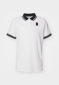 Valkoinen lyhythihainen polo-paita mustalla kauluksella ja hihansuu-bandilla, kaksi nappia ja pieni musta ja punainen Nike-logo vasemmassa rinnassa.