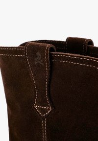 Bruine suède laars met een zachte textuur, voorzien van lichtgekleurde stiksels en een kleine aantreklus aan de bovenkant. Schedellogo is vaag zichtbaar.