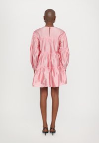 Ροζ σατέν φόρεμα με μακριά φουσκωτά μανίκια, διαβαθμισμένες ρυτίδες και άνοιγμα σε σχήμα κλειδαριάς στην πλάτη. Λείο, απαλό υλικό και μήκος πάνω από το γόνατο.