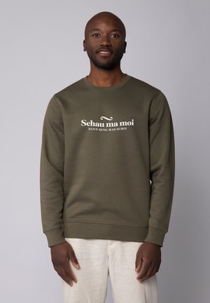 Olivgrüner Sweatshirt aus weichem Stoff, mit dem auffälligen weißen Text "Schau ma moi" quer über die Brust. Runder Ausschnitt und gerippte Bündchen.