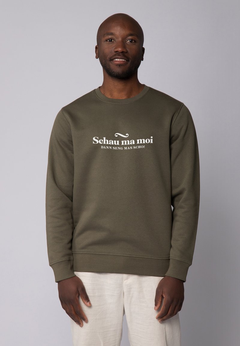 Olijfgroene sweatshirt van zacht materiaal, met grote witte tekst "Schau ma moi" over de borst. Ronde halslijn en geribde manchetten.