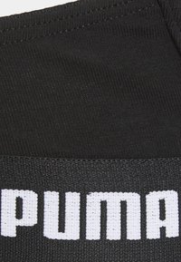 Black elastic waistband featuring raised white text that reads "PUMA." The fabric texture is smooth with a slight sheen.