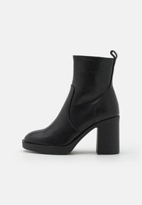 Bottine en cuir noir avec talon bloc, bout arrondi, et une languette à l'arrière, présentée sur un fond blanc uni.