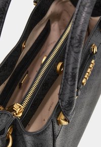 Czarna torebka z textured zewnętrzną stroną, złotymi akcentami i kieszenią zabezpieczoną zamkiem. Wnętrze z jasnym materiałem wykończeniowym.