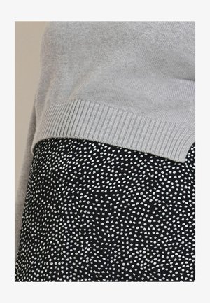 Hall, soonik servaga kampsun koos musta seelikuga, millel on valged täpilised mustrid, rõhutades kontrastseid tekstuure ja mustreid.