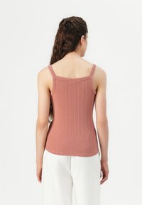 Ribbed tank top in a dusty rose color, featuring slim straps and a fitted design. Made of a soft, stretchy fabric with a smooth texture.
