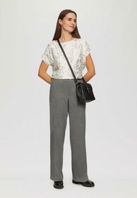 Haut à motif métallique léger avec des manches courtes, associé à un pantalon gris taille haute et un petit sac à bandoulière noir. Chaussures noires.
