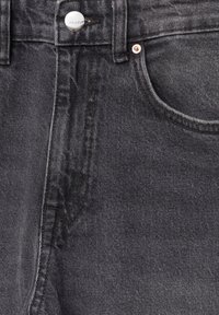 Gros plan sur un jean en denim noir montrant la poche avant, la passants de ceinture, la couture de la fermeture éclair et un bouton argenté avec le logo "Pull&Bear".