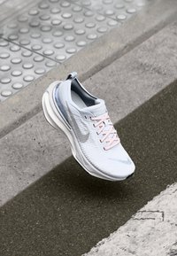 Baskets de course Nike bleu clair avec des lacets roses, tige texturée, semelle rembourrée et logo discret. Design arrondi, adapté à un usage athlétique.