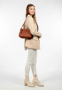 Sac en cuir marron avec une finition texturée, quincaillerie en argent et une bandoulière, associé à un blazer beige cintré et un pantalon blanc.