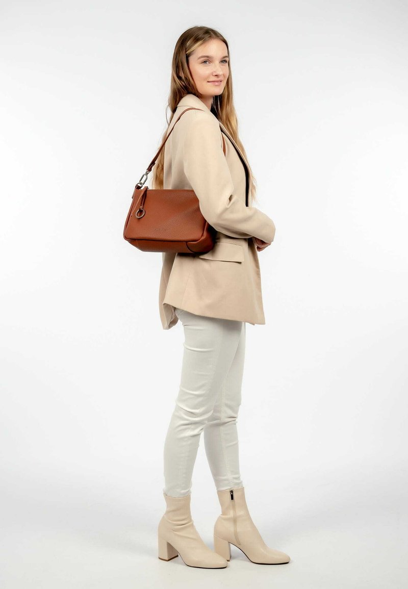 Sac en cuir marron avec une finition texturée, quincaillerie en argent et une bandoulière, associé à un blazer beige cintré et un pantalon blanc.
