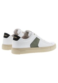 Zapatillas de cuero blancas con un panel lateral de ante verde, suela de goma beige y acento de logo negro en el talón con texto dorado.