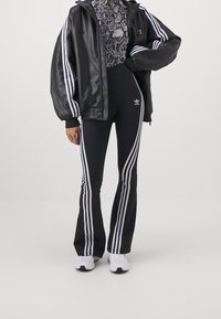 Svart faux läderjacka med vita ränder, tillsammans med högmidjade svarta utsvängda byxor med sidostripes. Innehåller en mönstrad topp.