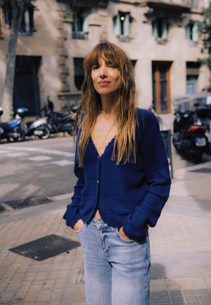 Cardigan bleu en tricot avec col en V et fermeture à boutons, associé à un jean en denim clair dans un cadre extérieur décontracté.