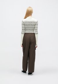 Svetre s dlhým rukávom v krémovej farbe s čiernymi geometrickými vzormi; skombinované s hnedými širokými nohavicami s bočnými vreckami a elastickým pásom.