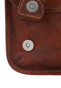 Brun lædertaske hjørne med synlige syninger og en sølvmetal snaplukning. Teksturen virker glat med lille korndetaljering.