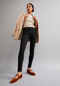 Jean noir, top crème côtelé, blazer beige et chaussures en velours marron. Le blazer a un bouton unique, et les chaussures présentent un design découpé.
