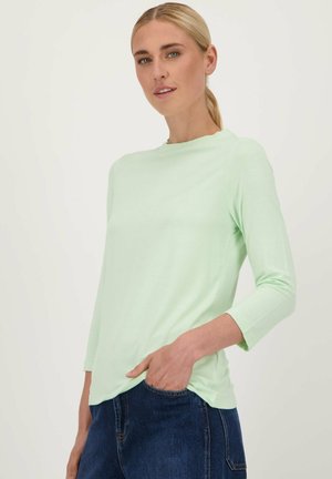 Haut à manches longues vert menthe clair avec un col rond, texture lisse et fentes sur les côtés, associé à un jean en denim bleu foncé.