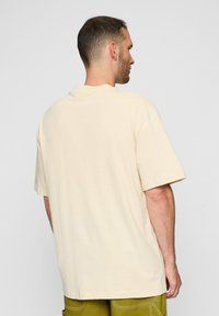 Világos bézs, oversized pamut póló, kerek kivágással és rövid ujjal, sima, puha textúrával.