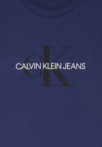 Camiseta de algodón azul marino con el texto "CALVIN KLEIN JEANS" en blanco, con un gran logo negro "CK", cuello redondo y mangas cortas.