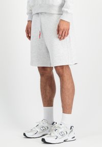 Šedé šortky z bavlnenej zmesi s elastickým pásom a nastaviteľnou šnúrkou. Nosia sa s bielymi teniskami a ponožkami po členky.