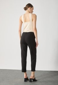 Svarte skreddersydde bukser med cropped passform, kombinert med en lys beige ermeløs topp med brede skulderstropper. Glatt tekstur.