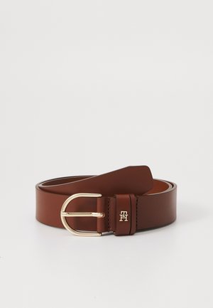 Ceinture en cuir marron avec boucle arrondie dorée et petit logo gravé sur la boucle de ceinture, enroulée sur fond blanc.