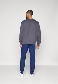 Grauer Sweater mit Rundhalsausschnitt, passende blaue Jogginghose und weiße Sneaker. Schlichtes Design, weicher Stoff und lässige Passform.