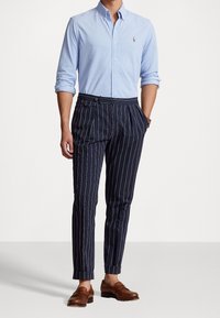 Jasnoniebieska koszula na guziki z kołnierzykiem, granatowe spodnie w paski i brązowe mokasyny. Spodnie mają dopasowany krój i mankiety na nogawkach.