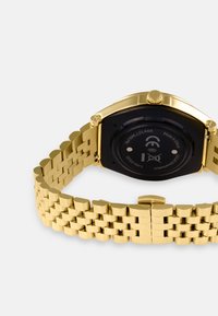Gold metal wristwatch with an octagonal case, black dial, and a textured, woven bracelet. Features a smooth clasp and a prominent crown.