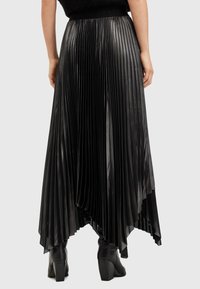 Black, pleated skirt with a flowy design and asymmetrical hem. Made from a shiny material, featuring a textured waistband.
